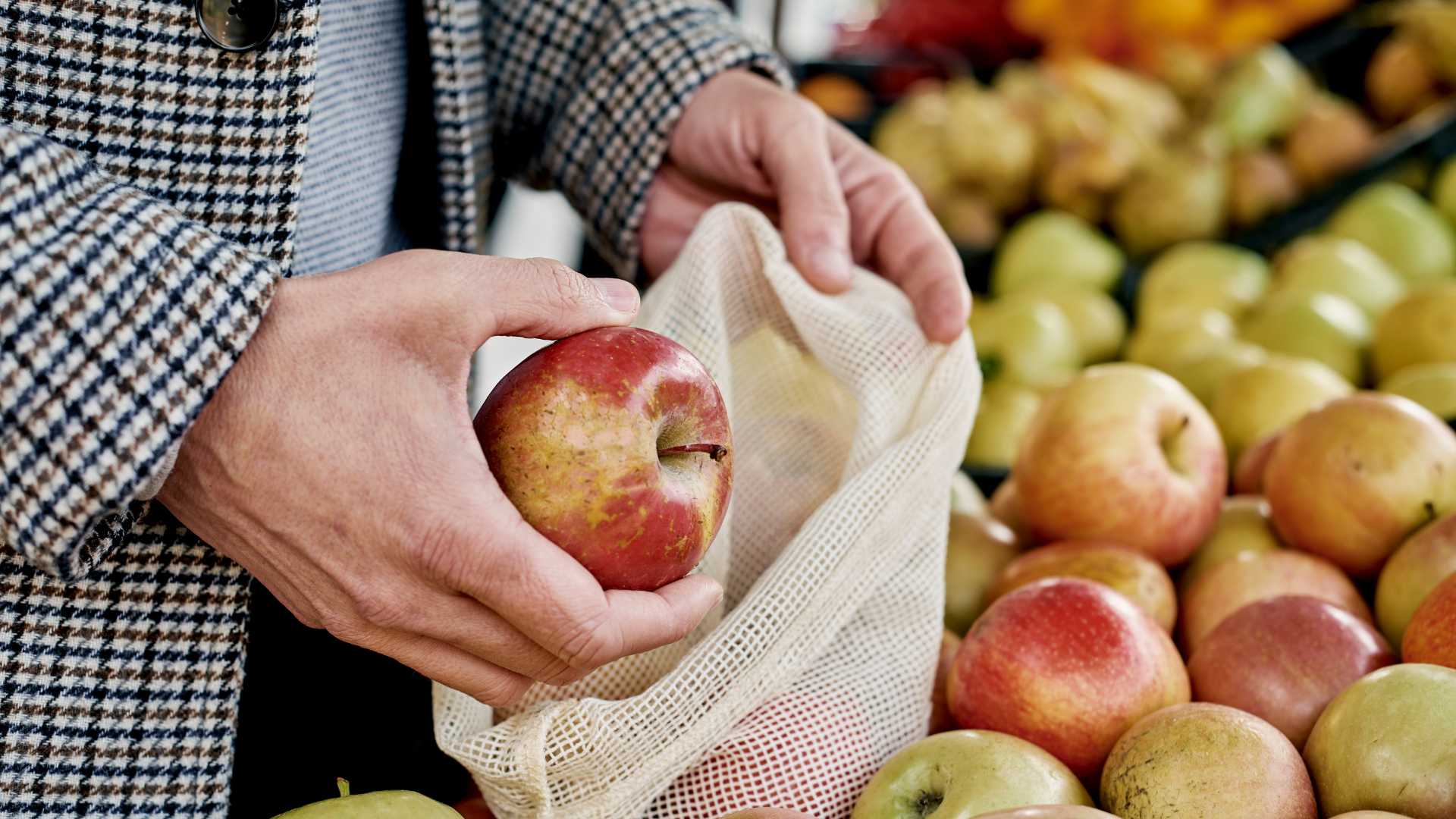 Homme qui achète ses pommes au marchand avec un sac en tissue 
